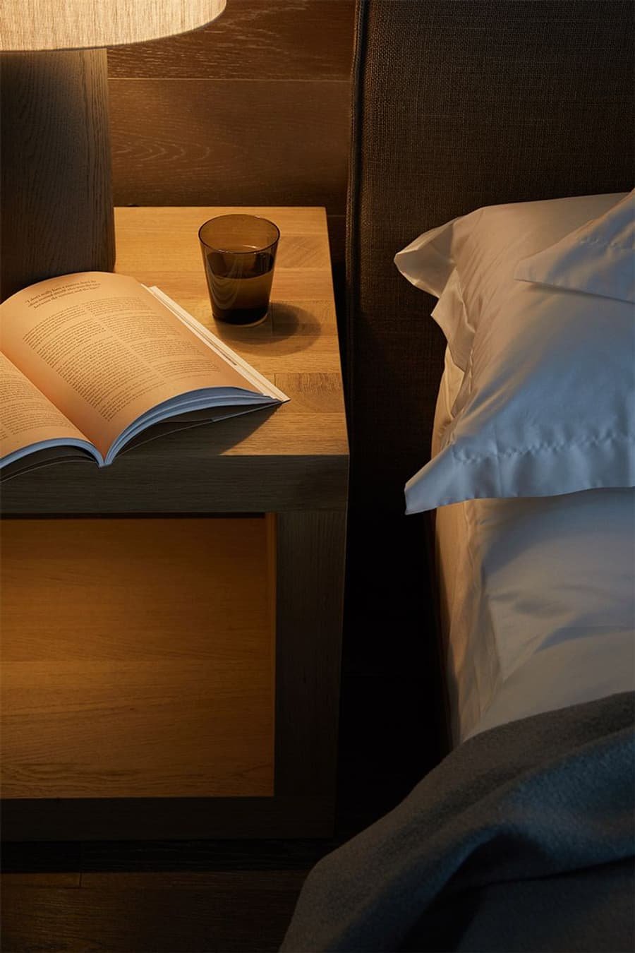 Criado-mudo com livro aberto e copo d’água ao lado da cama